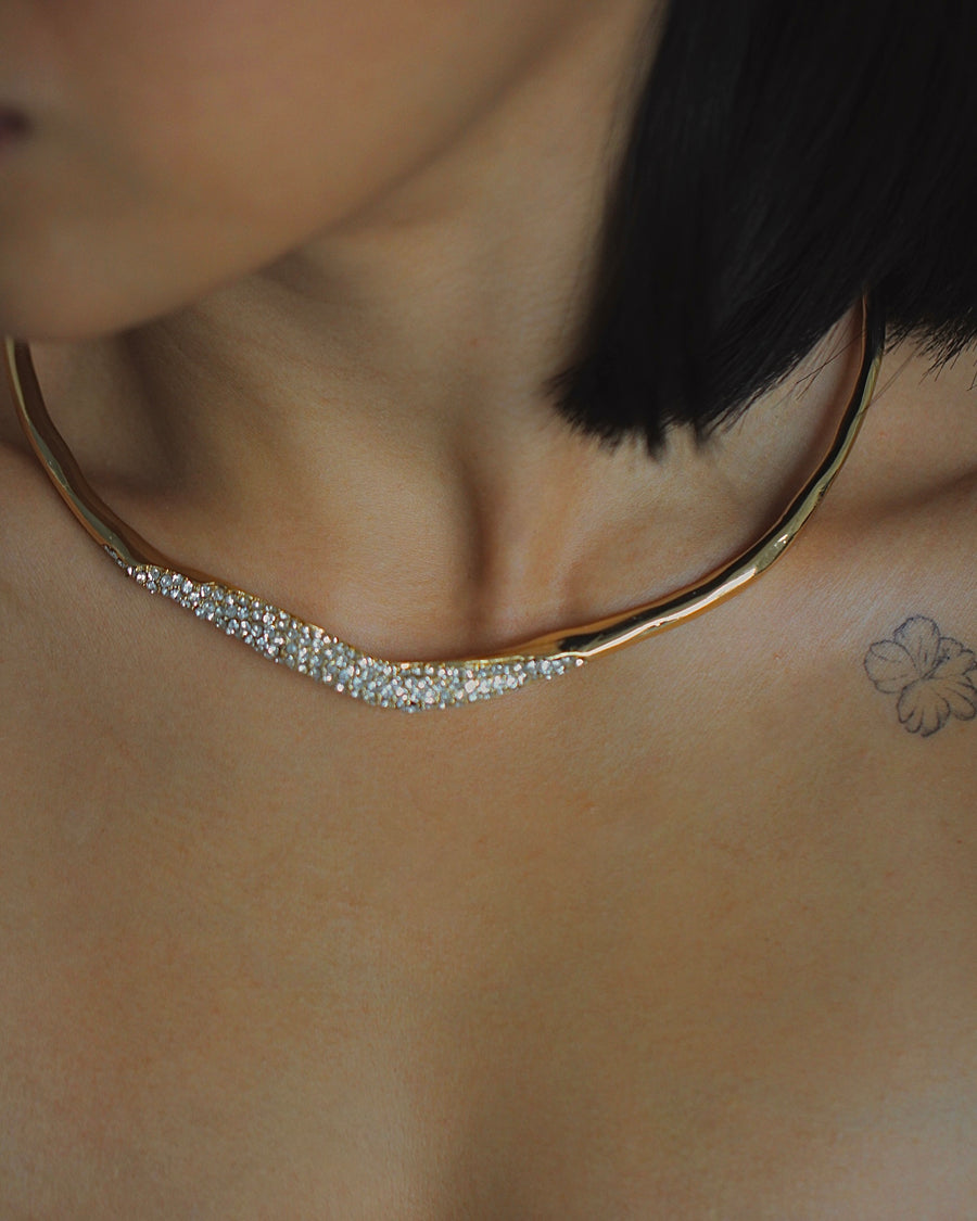 Close-up of a gold necklace with small stones on a person's neck.