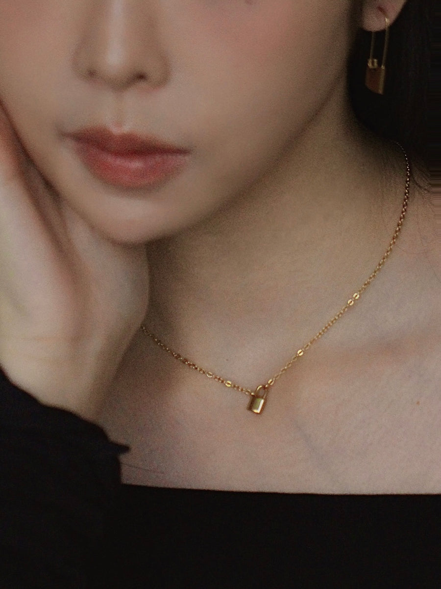 Close-up of a person wearing a gold necklace with a lock pendant.
