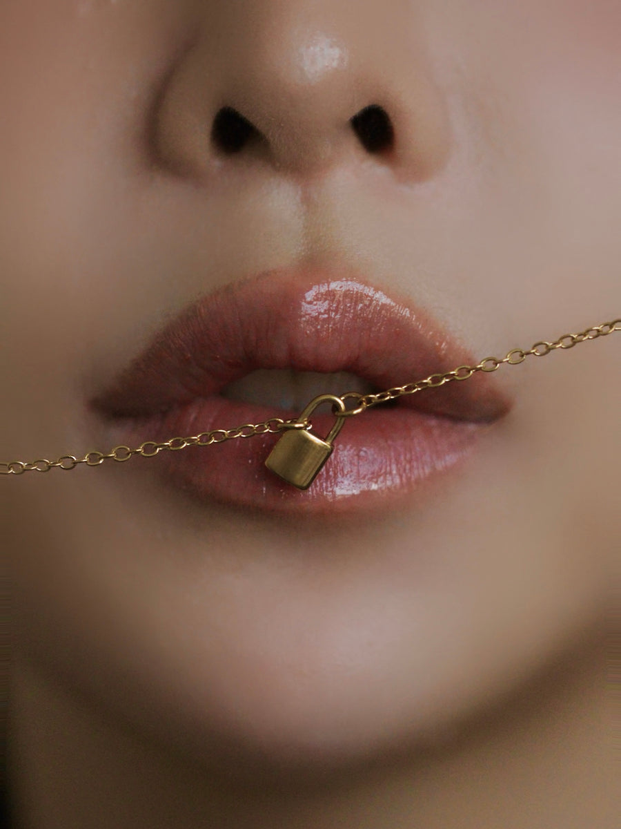 Close-up of a gold necklace with a lock pendant worn around the neck.